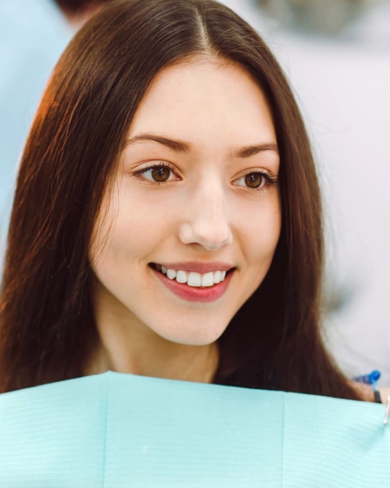 Patient admiring her clean, healthy smile in a hand mirror after a check-up at Alpha Dental, Sutera Utama