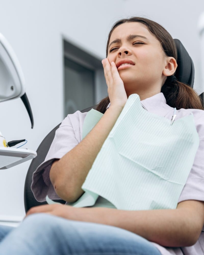 Patient holding her jaw in discomfort while seated in the dental chair at Alpha Dental, Sutera Utama